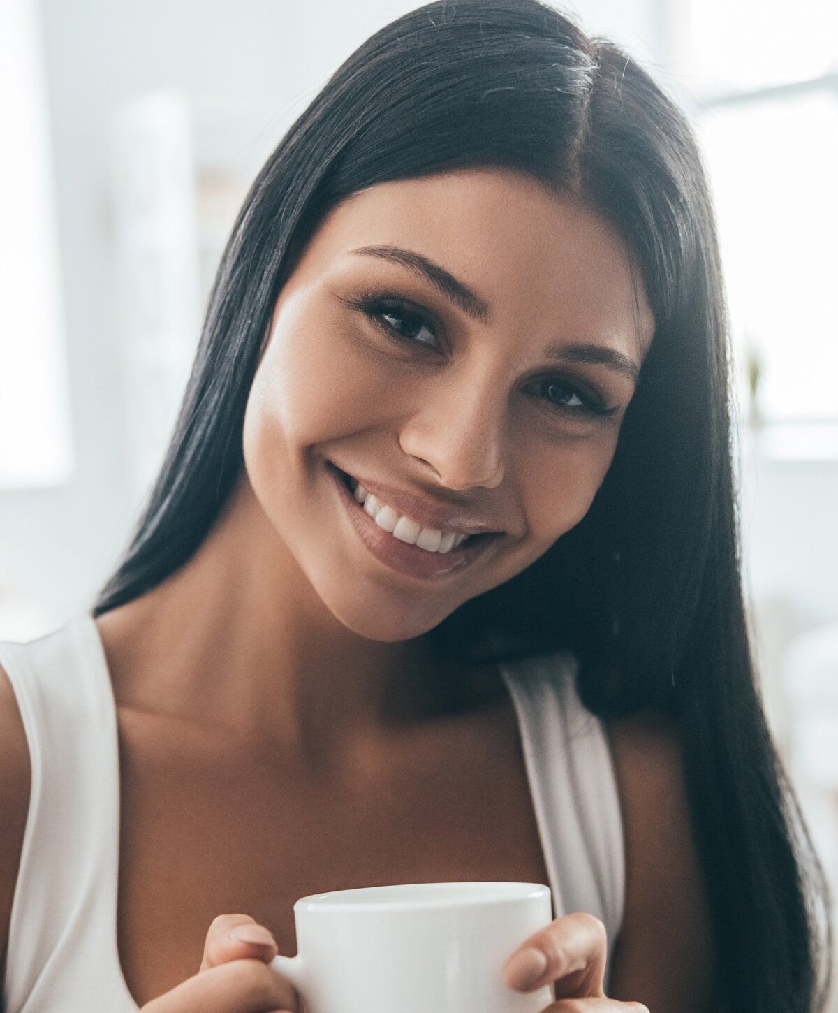 Smiling woman holding a cup, bright background.