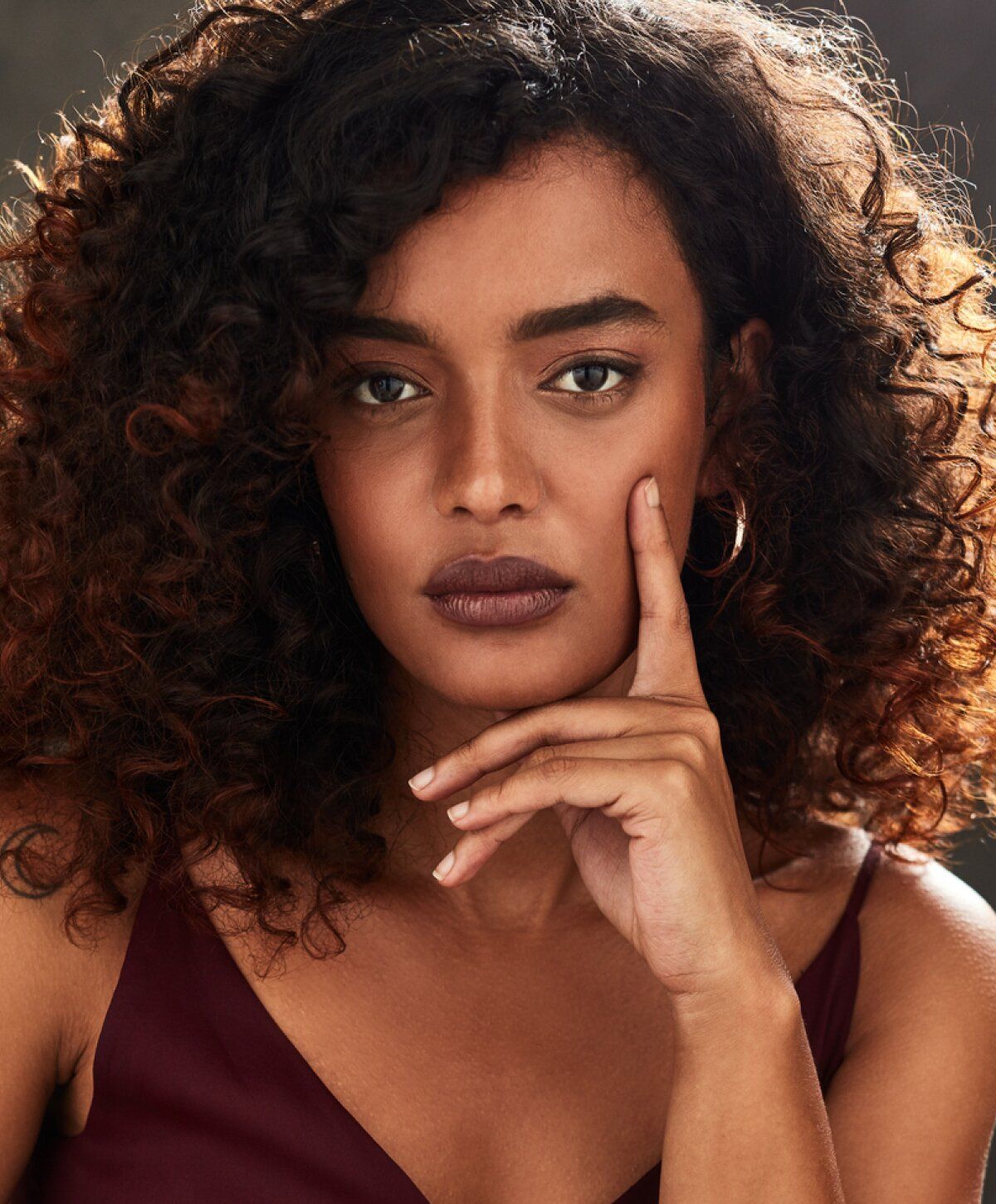 Woman with curly hair resting chin on hand.
