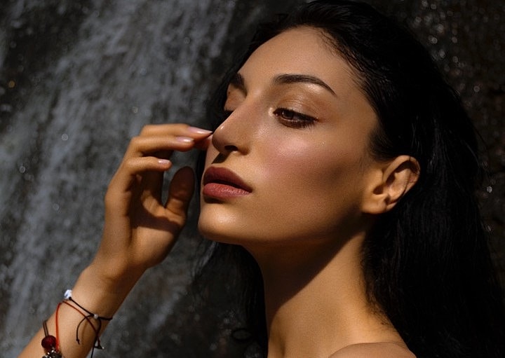 Woman touching her face against a stone backdrop.