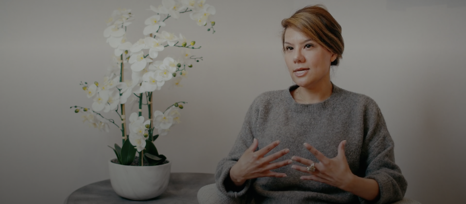 Woman speaking with floral arrangement in background.